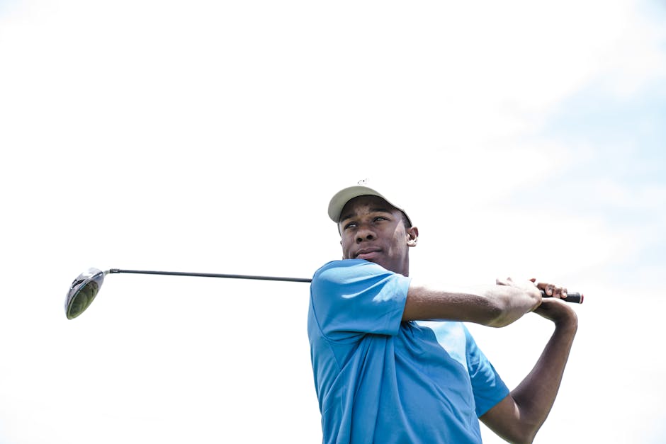 African American man playing golf against a bright sky, mid-swing.