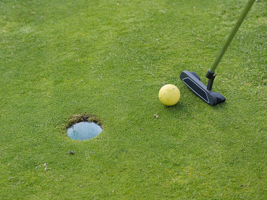 A golf ball and putter near a hole on a lush green golf course, ready for a putt.